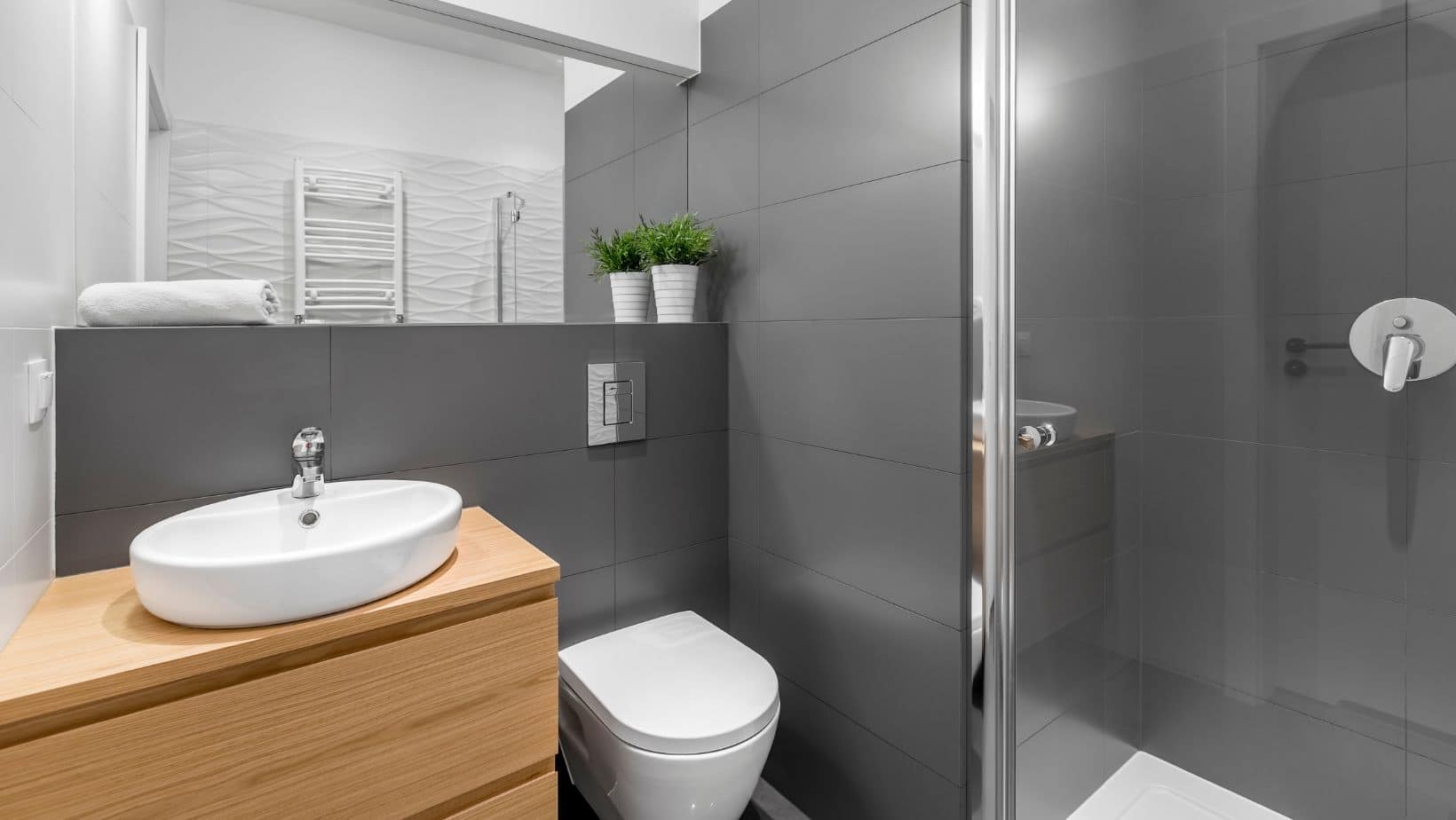 Small modern grey bathroom with wood bathroom cabinet, toilet, and shower