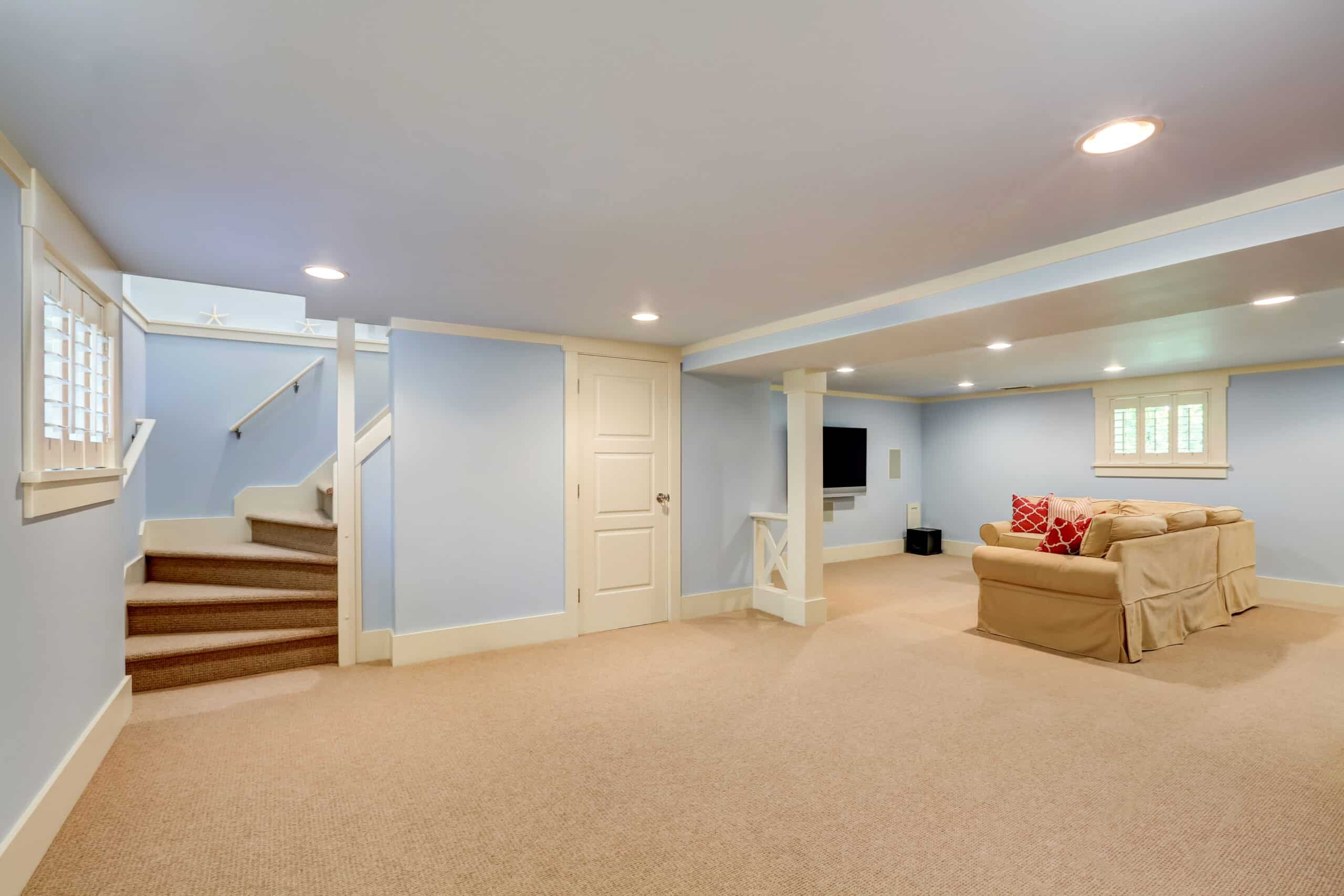 Spacious basement room interior in pastel blue tones. Beige carpet floor and large corner sofa with TV. Northwest, USA