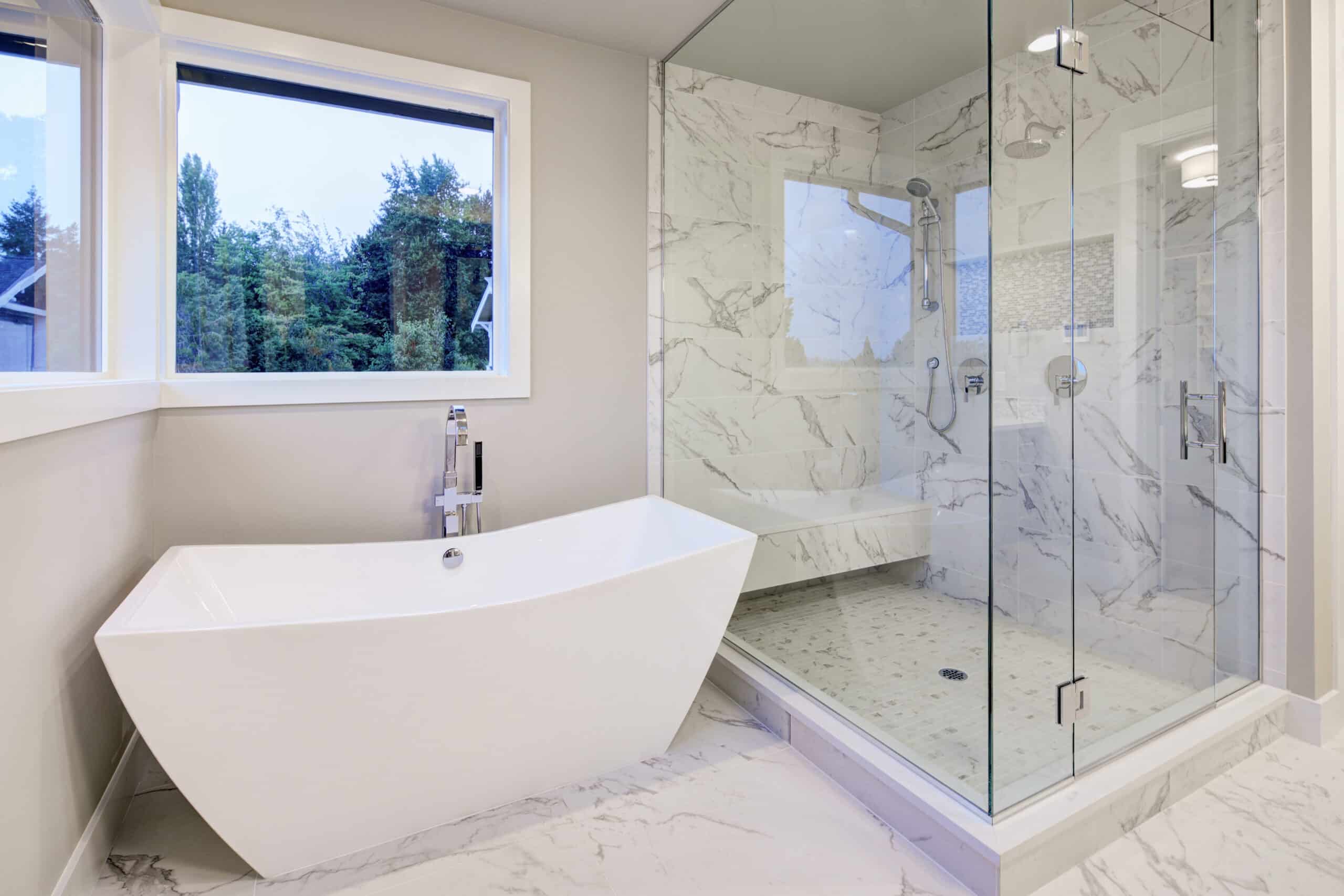 Sleek bathroom features freestanding bathtub atop marble floor placed in front of glass shower accented with rain shower head and gray and white marble surround. Northwest, USA