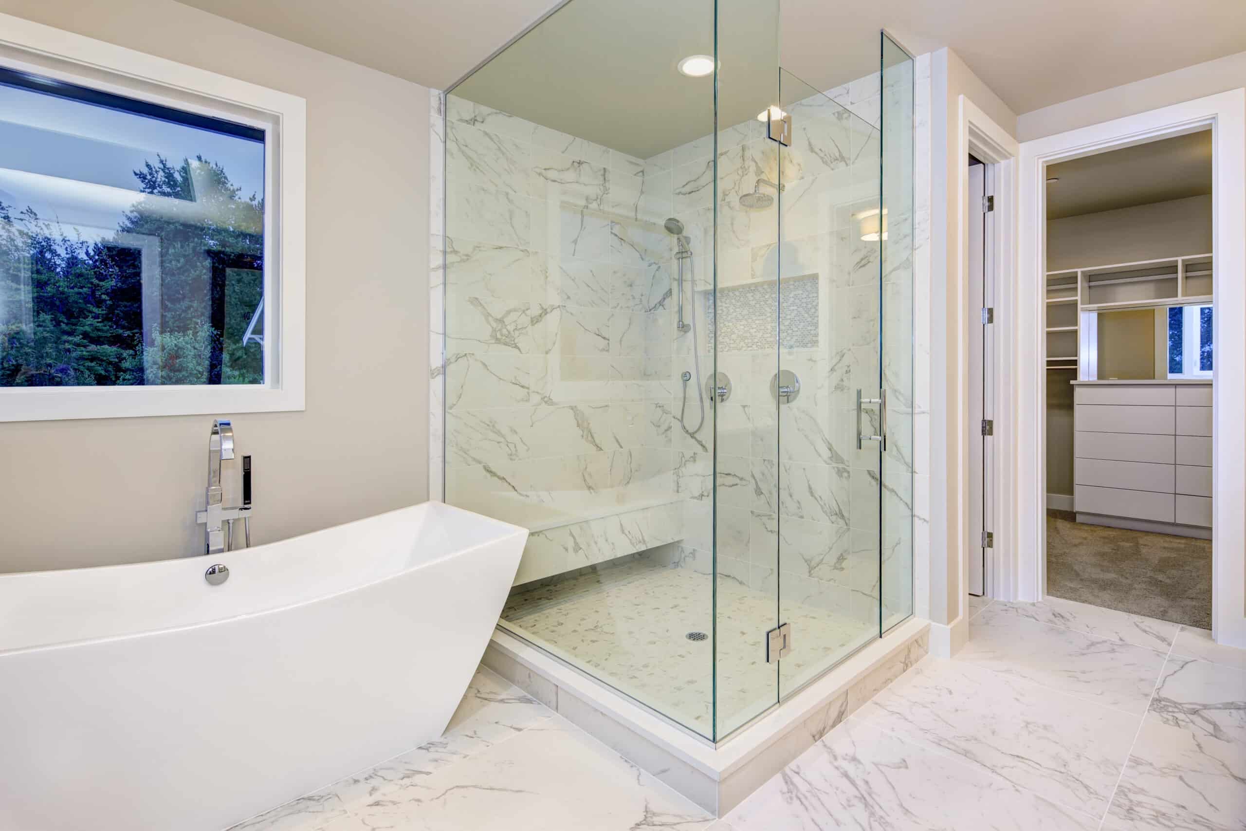 Sleek bathroom features freestanding bathtub atop marble floor placed in front of glass shower accented with rain shower head and gray and white marble surround. Northwest, USA