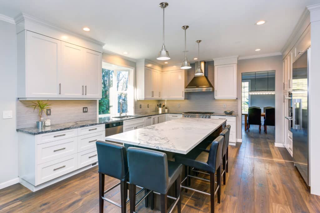 Luxury home interior boasts Beautiful white kitchen with custom white shaker cabinets, endless marble topped kitchen island