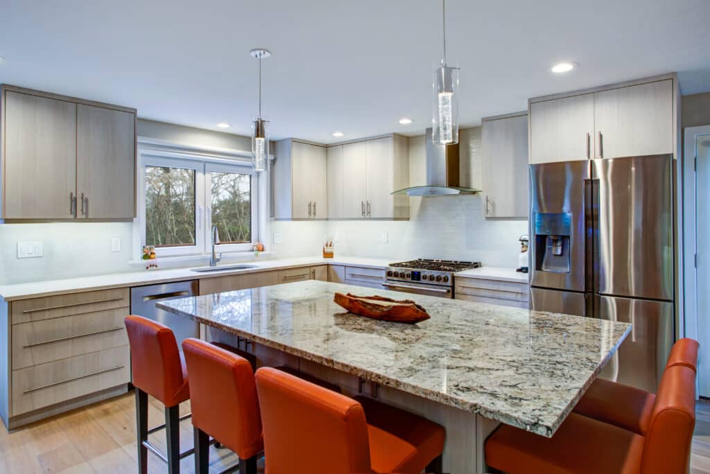 Gorgeous kitchen design features ivory kitchen cabinets flanking modern steel kitchen hood, linear marble tile backsplash, kitchen island with granite counter top and red leather barstools.
