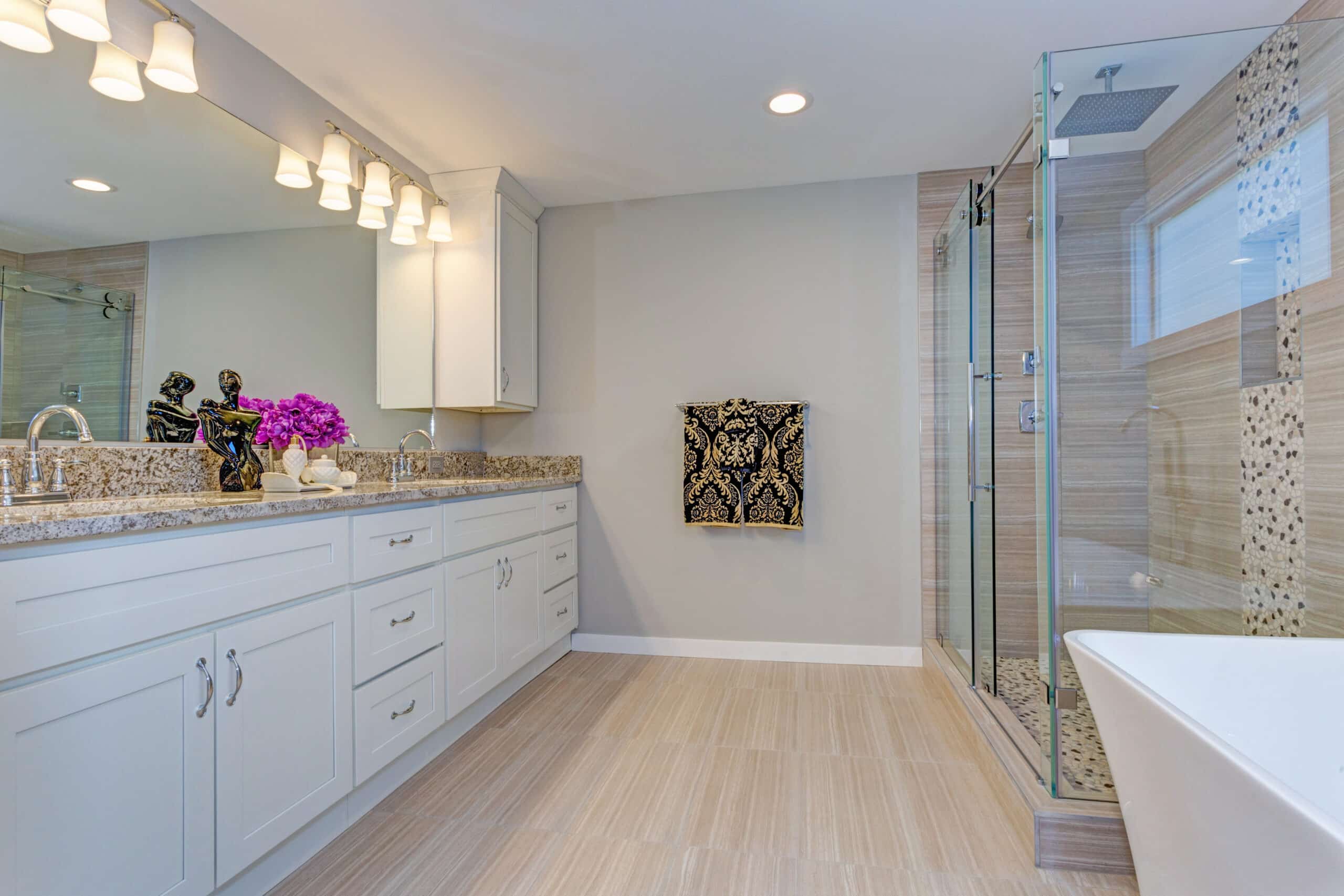 Luxurious bathroom style with big glass enclosed shower, a bath tub, and a modern white shaker double-sink vanity with brown countertop