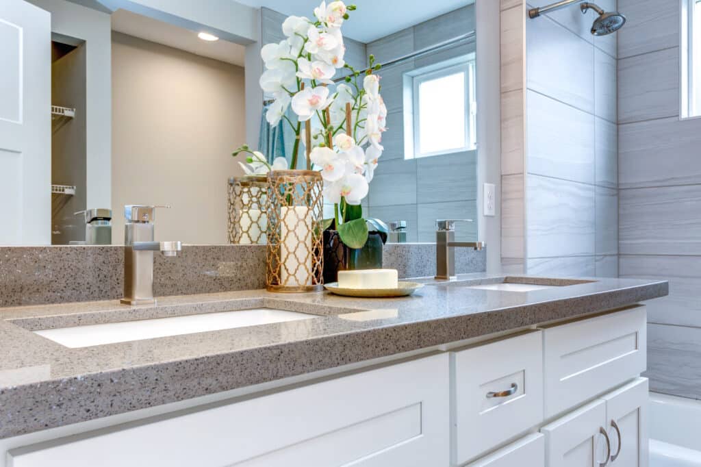 Zoomed in photo of a white shaker double-sink vanity with grayish marble countertop, and a bath-tub with shower beside it.