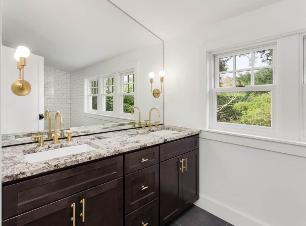 White bathroom with dark brown double-sink vanity and a beige granite countertop with gold hardware