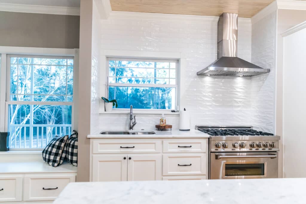 Large renovated white kitchen with updated cabinets, textured subway tile, black iron lights and pine hardwood flooring.