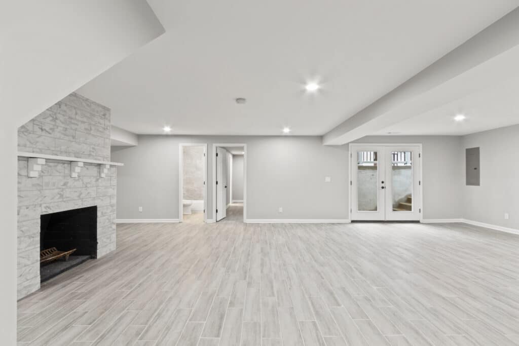 Bright, spacious light grey basement with fireplace, light wood flooring and light gray walls.