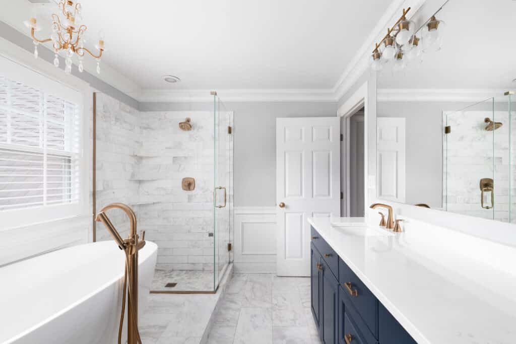 Clean sleek, and luxurious white bathroom with navy blue vanity, white countertop, a corner enclosed shower, and a bath tub.