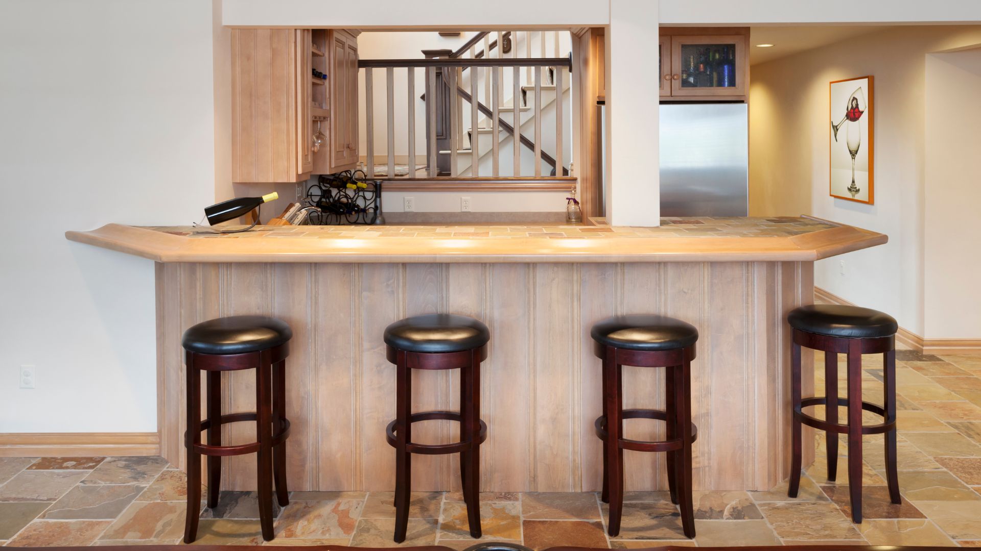 Basement bar beside stairs in light wood cabinet and cream countertop