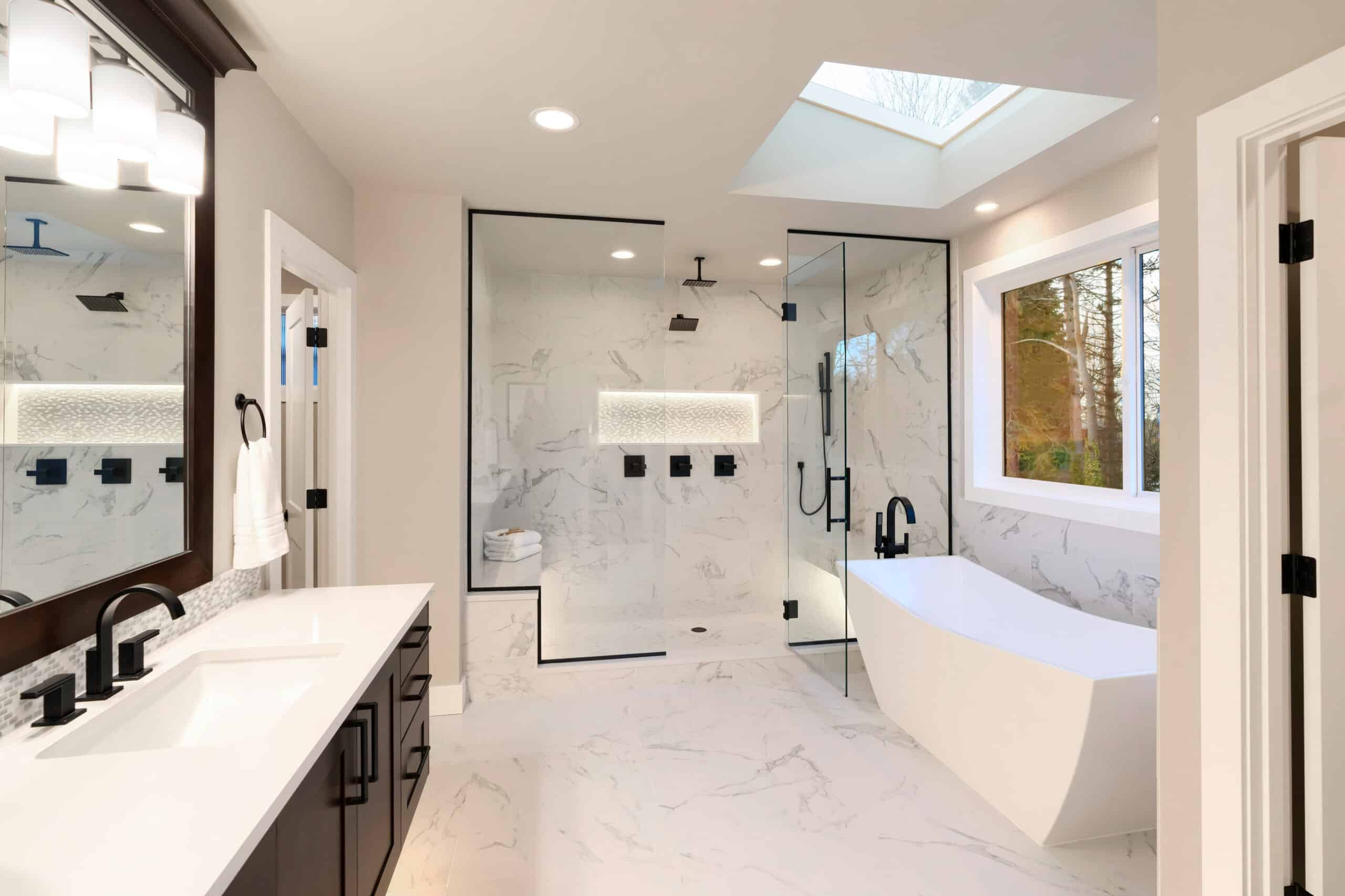 Luxury contemporary home bathroom interior with dark brown cabinets, white marble, walk in shower, free standing tub, two mirrors, flowers.