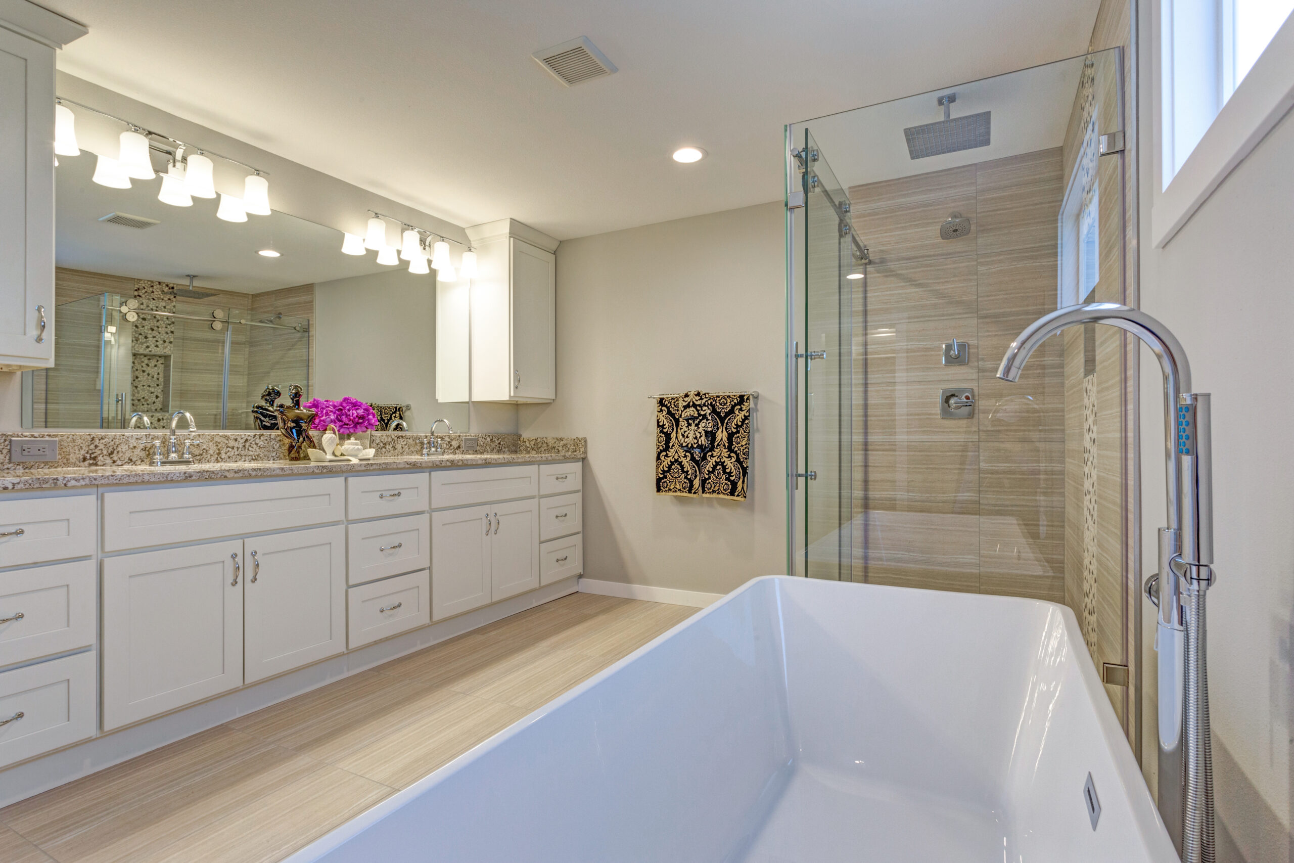 Light modern bathroom design with long dual vanity cabinet, glass shower and freestanding tub.