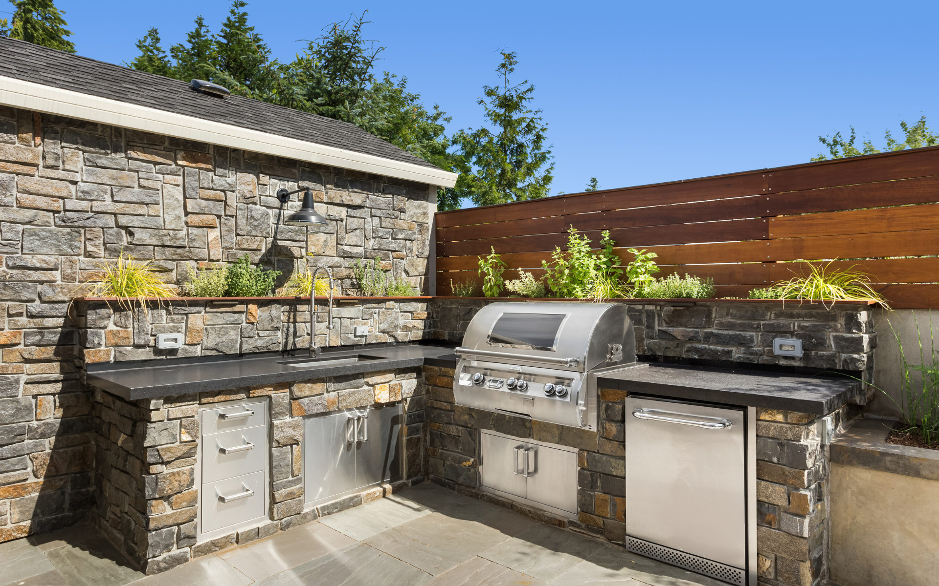 Outdoor kitchen made of bricks, with stainless drawers and cabinets, and dark gray countertop