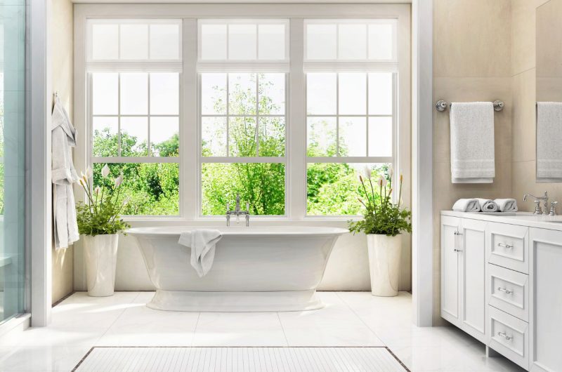 White modern bathroom cabinets with bath tub in the middle, having plants behind it for relaxing feels