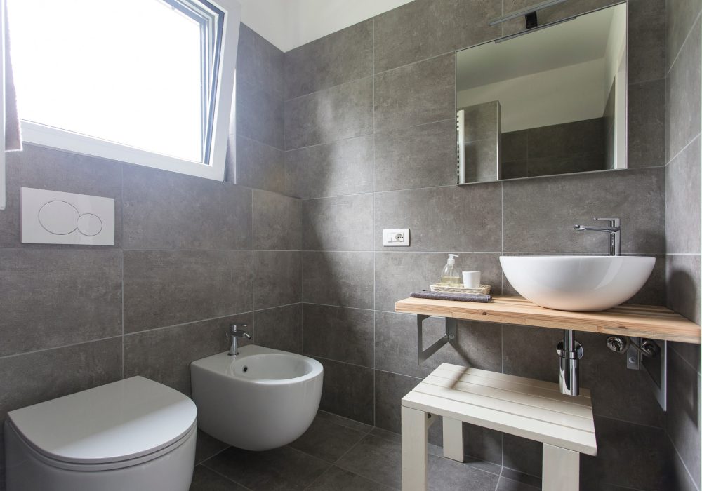 Dark brown bathroom design with a floating toilet, wall mounted sink, and a pedestal vanity surrounded by slate tiles